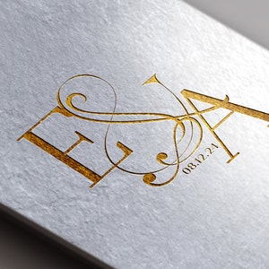 Peut inclure: Lettres "EA" en feuille d'or avec une fioriture décorative et la date "08.12.24" sur un fond blanc.