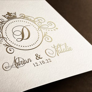 May include: A gold-colored wedding invitation with a decorative monogram featuring the letter "D" and a crown. The text "Adrian & Natalie 12.10.22" is written in cursive below the monogram.