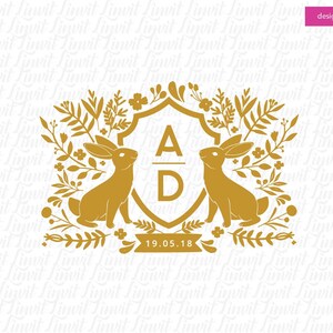 以下が含まれることがあります： 「A D」のイニシャルと「19.05.18」の日付が刻まれた金色の盾。両側にウサギが2匹いる花柄のデザインで囲まれています。