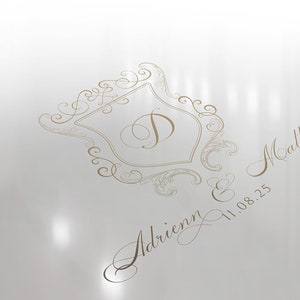 May include: A white background with a gold ornate design featuring a shield with the letter "D" inside. The text "Adrienn & Matthew 11.08.25" is written in cursive below the design.