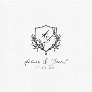 May include: A black and white wedding monogram with a shield and floral wreath. The initials "A & D" are inside the shield. The text "Arthur & Daniel 08.12.22" is below the monogram.