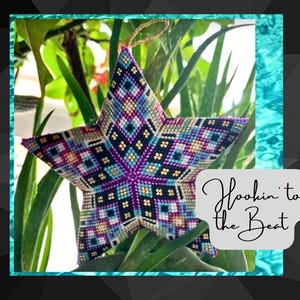 May include: A colorful star-shaped ornament with a geometric pattern in shades of purple, blue, gold, and black. The ornament is hanging from a green plant and has the text "Hookin' to the Beat" written on the right side of the image.