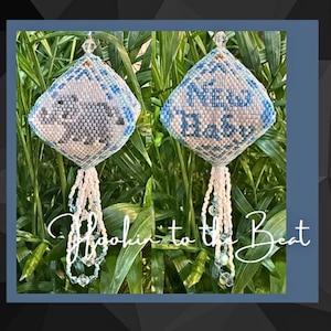 Op de afbeelding: Twee blauwe en witte kralenversieringen met een witte kwast. Een versiering heeft een grijze beer en de andere zegt "Nieuwe Baby".