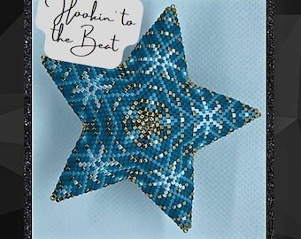Pode incluir: Um ornamento de estrela azul turquesa com contas, com um padrão geométrico branco e dourado. O ornamento está sobre um fundo azul claro com um cartão branco que diz "Hookin' to the Beat".