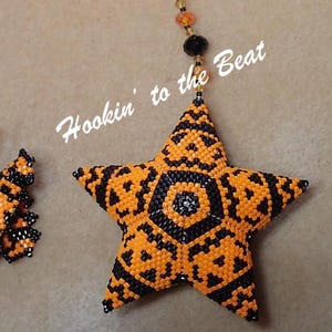 May include: Three Halloween-themed beaded ornaments: a star, a butterfly, and a diamond. The star is orange and black with a jack-o'-lantern face design. The butterfly is orange and black with a jack-o'-lantern face design. The diamond is orange and black with a jack-o'-lantern face design. The text "Hookin' to the Beat" is written in white on a brown background.