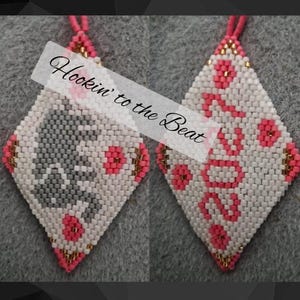 Op de afbeelding: Twee ruitvormige kralenornamenten met witte, roze, grijze en gouden kralen. Het linker ornament toont een grijs silhouet van een kat met roze accenten, terwijl het rechter ornament de tekst 2020 in roze kralen toont. Tekst luidt Hookin' to the Beat.