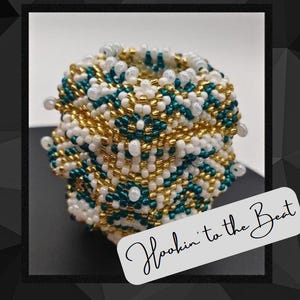 Op de afbeelding: Een geperst, veelkleurig, geometrisch figuur met een wit, goud en teal kleurenschema. De vorm is gemaakt van kleine kralen en heeft een textuur. De tekst "Hookin' to the Beat" is geschreven in cursief op een witte achtergrond.