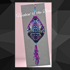 May include: A beaded ornament with a geometric design in shades of purple, blue, and gold. The ornament is suspended from a silver chain and has a long, beaded tassel.