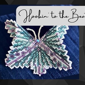 Könnte beinhalten: Eine Brosche in Form eines Schmetterlings aus Perlen in Grün, Weiß und Lila. Der Schmetterling hat ein detailliertes Design und eine glitzernde Mitte. Der Text "Hookin' to the Beat" ist in Kursivschrift über dem Schmetterling geschrieben.