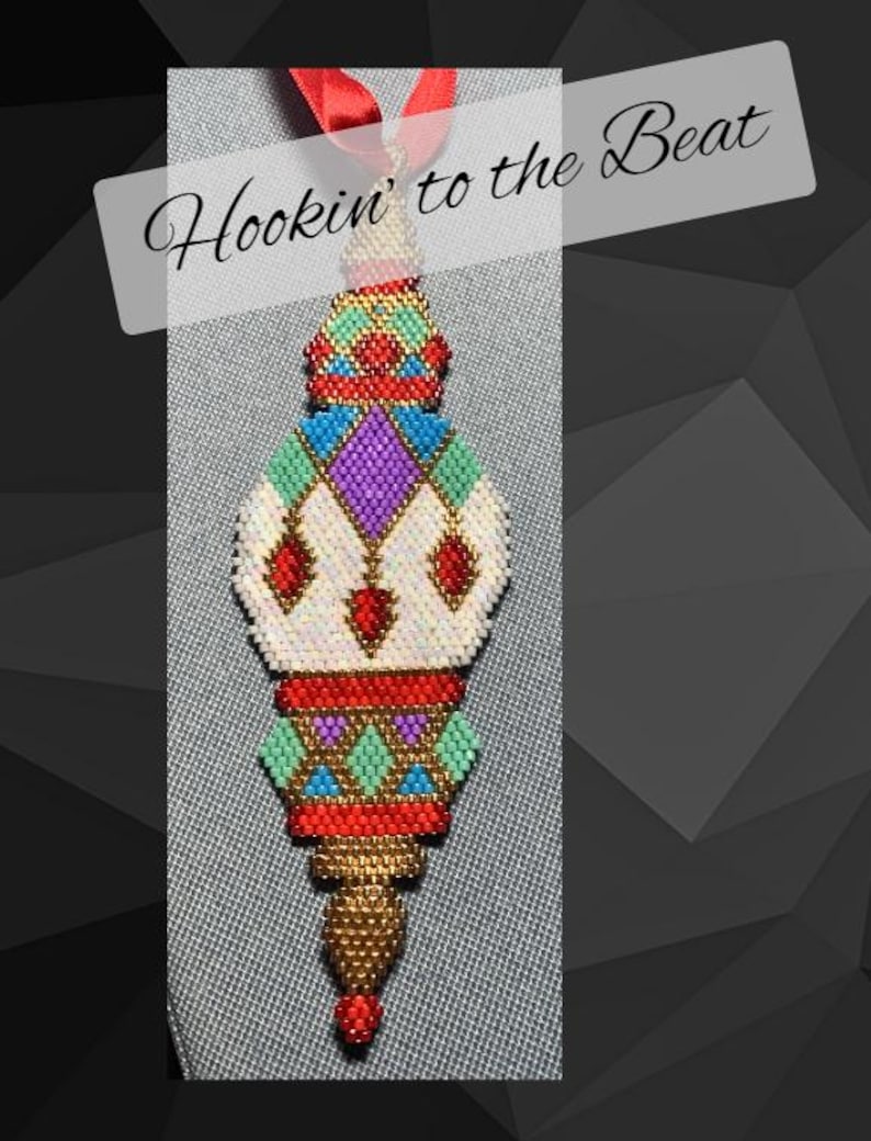 May include: A colorful beaded ornament with a geometric design. The ornament is red, white, gold, blue, green, and purple. The ornament is hanging from a red ribbon and has the text "Hookin' to the Beat" above it.