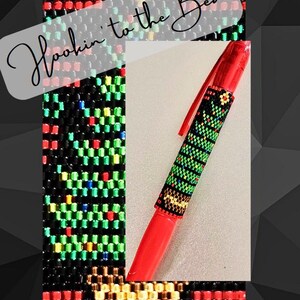 May include: A red pen with a green, red, yellow and black beaded design of a Christmas tree. The text "Hookin' to the Beat" is written in white on a black background.