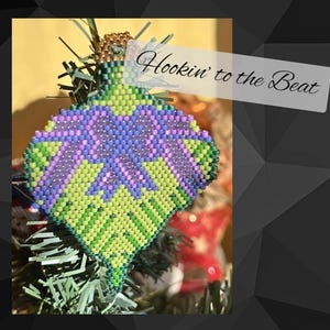 Puede incluir: Un adorno de Navidad de cuentas verdes y moradas con forma de hoja con el texto "Hookin' to the Beat" en un árbol de Navidad.
