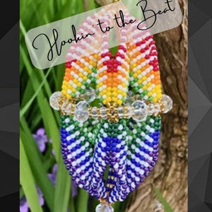May include: A rainbow-colored beaded ornament with the text "Hookin' to the Beat" in a white box. The ornament is made of small beads and has a crystal-like bead at the bottom.