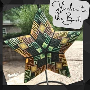Könnte beinhalten: Ein sternförmiger Wandbehang in Grün, Schwarz und Gold mit geometrischem Muster. Der Stern steht auf einem Metallständer und der Text "Hookin' to the Beat" ist auf einem weißen Etikett geschrieben.