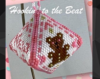 Pode incluir: Um ornamento de contas rosa e branco em forma de pirâmide com um desenho de urso marrom. O ornamento tem o texto "Hookin' to the Beat".