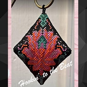 May include: A beaded, diamond-shaped pendant with a floral design in shades of pink, orange, and green, set against a black background. The pendant is attached to a gold-colored ring. The text "Hookin' to the Beat" is written in white cursive.