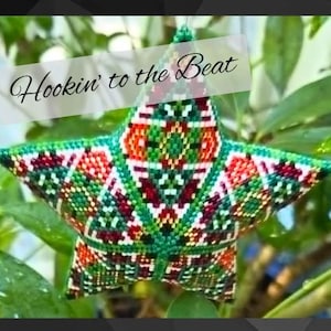 May include: A handcrafted, five-pointed star ornament with a colorful, geometric pattern. The star is primarily green, with accents of red, orange, and white. The text "Hookin' to the Beat" is displayed across the top of the star.