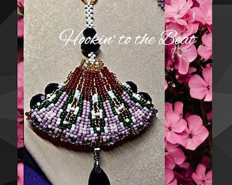 May include: A beaded fan-shaped pendant with a black teardrop charm. The pendant is made with red, green, white, and purple beads. The text "Hookin' to the Beat" is visible in the image.