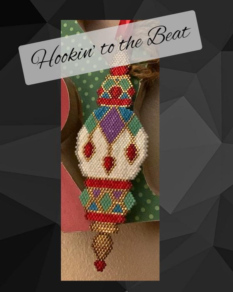 May include: A colorful beaded ornament with a geometric design. The ornament is white, red, green, gold, and purple. The ornament has a gold tassel at the bottom. The text "Hookin' to the Beat" is written on a white background.