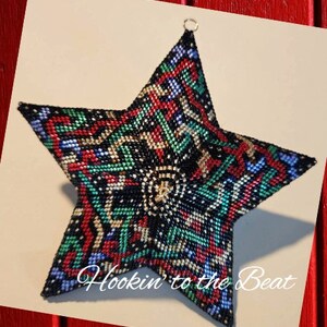 May include: A black, green, red, and blue beaded star ornament with a gold bead in the center. The star is 3D and has a geometric pattern. The text "Hookin' to the Beat" is written below the star.