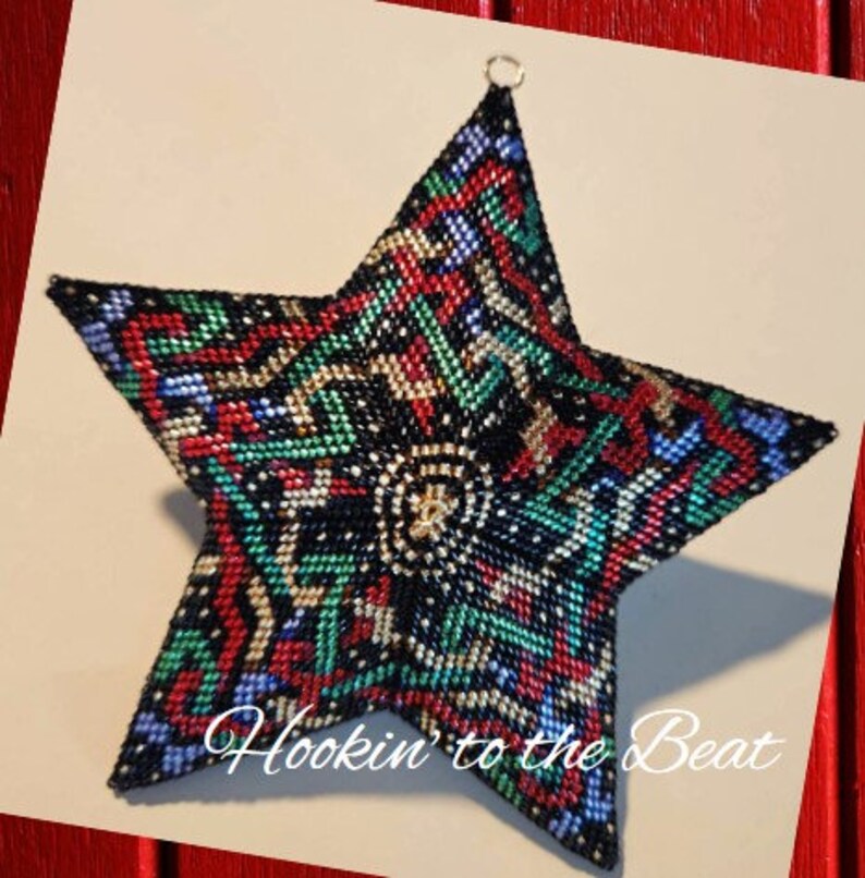 May include: A black, green, red, and blue beaded star ornament with a gold bead in the center. The star is 3D and has a geometric pattern. The text "Hookin' to the Beat" is written below the star.