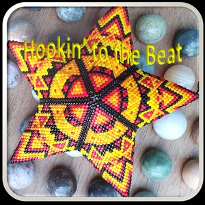 Könnte beinhalten: Ein sternförmiger Perlenschmuck mit einem geometrischen Muster in Rot, Gelb und Schwarz. Der Schmuck ist von glatten, runden Steinen umgeben. Der Text "Hookin' to the Beat" ist in gelben Buchstaben auf dem Schmuckstück geschrieben.