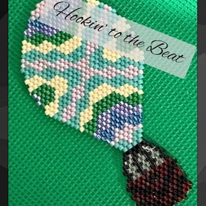 May include: A beaded hot air balloon design in shades of teal, green, yellow, and purple, with the text "Hookin' to the Beat" on a transparent banner. The balloon has a dark brown and black base, set against a green background.