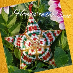 May include: A star-shaped ornament made of beads in red, white, green, and gold colors. The ornament is hanging from a green plant with white flowers. The text "Hookin' to the Beat" is visible in the image.
