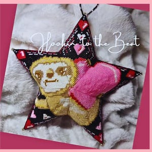 May include: A black star-shaped cushion with a pink heart and a sloth design. The cushion has the text "Hookin to the Beat" on it.