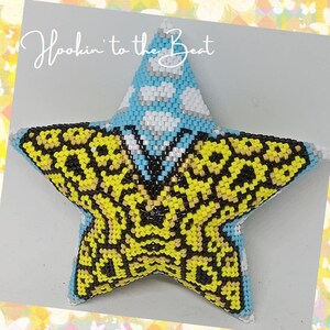 May include: A yellow and black beaded star with a blue and white polka dot centre. The star is a handmade craft item and has the text "Hookin' to the Beat" written above it.