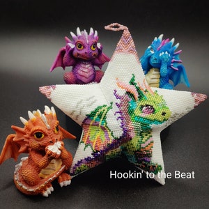 May include: A white star-shaped beaded ornament with a green, purple, and pink dragon design. Three small beaded dragons are attached to the star, one purple, one blue, and one orange.
