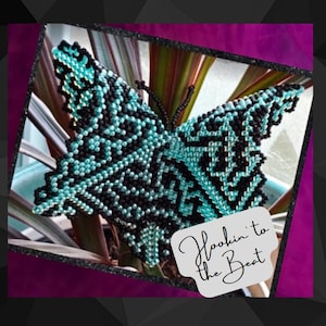 Op de afbeelding: Een turquoise en zwarte kralen vlinder met een wit label waarop "Hookin' to the Beat" staat.