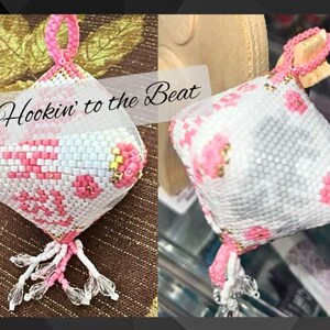Op de afbeelding: Hartvormig, met kralen bezet ornament in roze en wit, met de tekst "Hookin' to the Beat". Het heeft een roze lus en een kralenkwast. Gouden en transparante kralen accentueren het ontwerp. Een decoratief item.