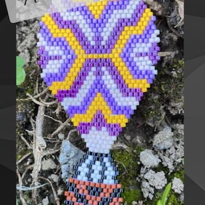 Pode incluir: Um amuleto de balão de ar quente em contas roxas, amarelas e brancas com o texto "Hookin' to the Beat".