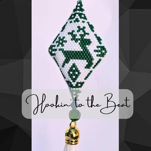 以下が含まれることがあります： 白と緑のビーズでできたオーナメントで、トナカイのデザインが施されています。オーナメントはダイヤモンド型で、白いタッセルがぶら下がっています。オーナメントの下には「Hookin' to the Beat」という文字が書かれています。