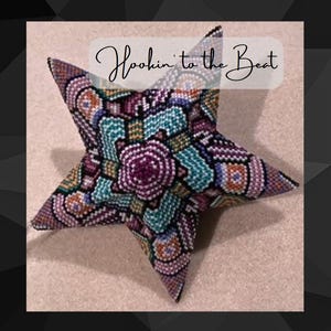 Peut inclure: Une étoile ornementale en perles multicolores avec un motif géométrique. L'ornement est fait de perles dans des tons de violet, bleu, vert, orange et blanc. Le texte "Hookin' to the Beat" est écrit en blanc sur un fond blanc.