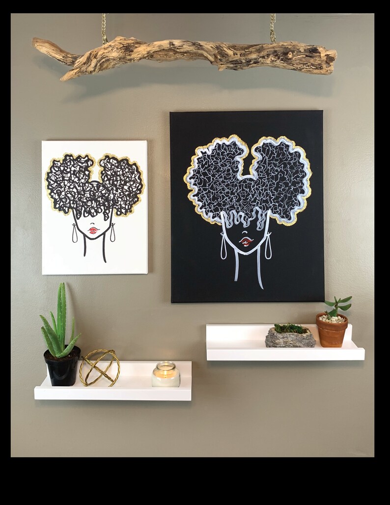 Puede incluir: Dos cuadros enmarcados de una mujer con un peinado afro. Los cuadros est&aacute;n en estantes blancos con una planta en maceta, una vela y una esfera decorativa. Un trozo de madera a la deriva cuelga del techo sobre los cuadros.