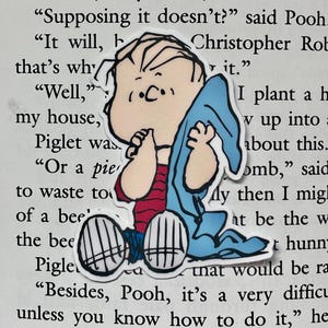 May include: A cartoon sticker of a young boy with brown hair wearing a red and white striped shirt, blue jeans, and a light blue blanket. The boy is sitting with his hands clasped in front of his face. The sticker is on a page of a book with text that reads "Supposing it doesn't?" said Pooh "It will, b that's why "Well," my house, Piglet was "Or a pie to waste to of a bee' the bee Pigle Christopher Rob it." I plant a h v up into about this. omb," said My then I mig at be the w t hunn that would be ra "Besides, Pooh, it's a very difficu unless you know how to do it," he
