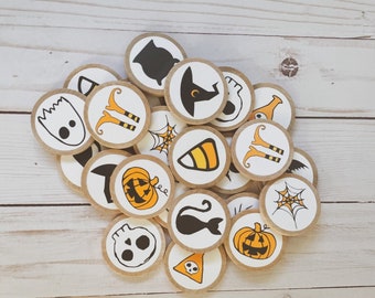 May include: A set of 18 Halloween-themed wooden circles with various images, including a witch's hat, a black cat, a ghost, a spider web, a pumpkin, and candy corn. The circles are arranged in a pile on a white wooden surface.