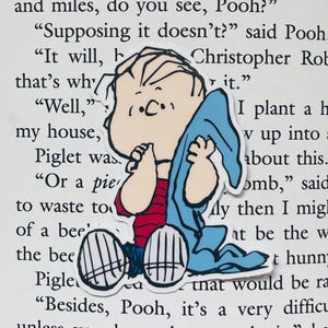 May include: A cartoon sticker of a young boy wearing a blue blanket and a red and white striped shirt. The boy is holding his hands together in front of his face. The sticker is on a white background with text.