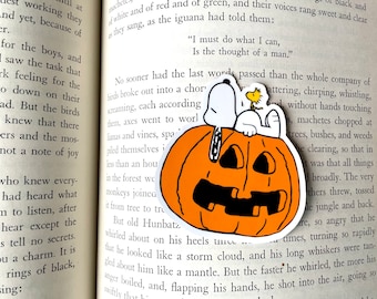 May include: Snoopy, the beagle from Peanuts, sits on top of a large orange jack-o'-lantern with a toothy grin.  Snoopy is wearing his signature red collar and is holding a small yellow bird in his paws.  The text "I must do what I can, Is the thought of a man." is printed on the page behind the sticker.