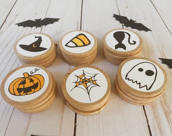 May include: Set of eight wooden Halloween themed game pieces. Each piece features a different Halloween icon, including a witch's hat, a candy corn, a black cat, a ghost, a pumpkin, a spider web, a bat, and a crescent moon.