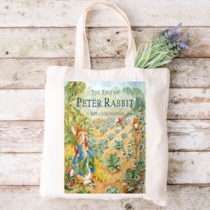 May include: A white canvas tote bag with a colorful illustration of Peter Rabbit from the book "The Tale of Peter Rabbit" by Beatrix Potter.
