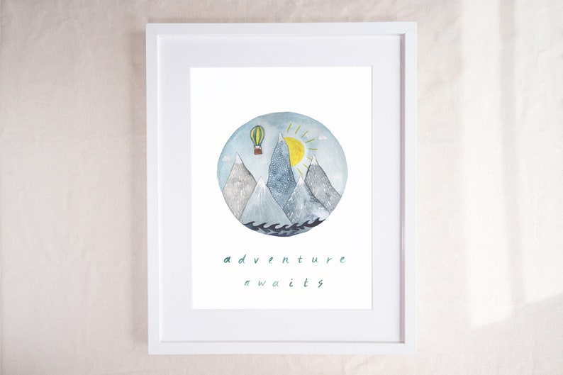 K&ouml;nnte beinhalten: Eine Aquarell-Illustration eines Hei&szlig;luftballons, der &uuml;ber eine Bergkette fliegt, mit einer Sonne, die am Himmel scheint. Die Illustration befindet sich in einem Kreis mit dem Text "adventure awaits" darunter.
