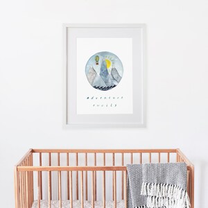 K&ouml;nnte beinhalten: Ein gerahmter Aquarelldruck mit einer blauen, grauen und gelben Illustration von Bergen, einem Hei&szlig;luftballon und einer Sonne. Der Text "adventure awaits" steht unter der Illustration.
