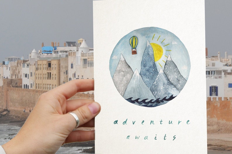 K&ouml;nnte beinhalten: Eine Aquarell-Illustration eines Hei&szlig;luftballons, der &uuml;ber Berge mit Sonne und Wellen fliegt. Der Text "adventure awaits" steht unter der Illustration.