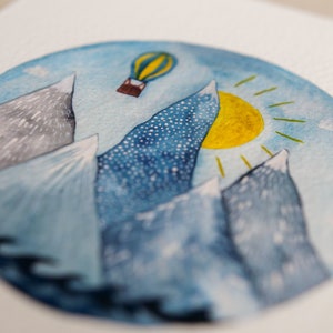 K&ouml;nnte beinhalten: Ein Aquarellbild eines blauen Himmels mit einer gelben Sonne und einem Hei&szlig;luftballon. Die Berge sind in Blaut&ouml;nen und Grau gemalt.