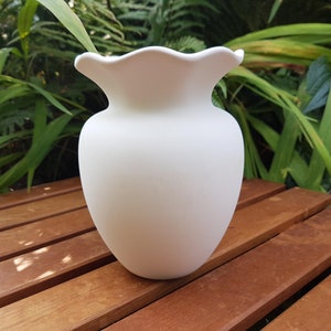 May include: A white ceramic vase with a scalloped rim. The vase is sitting on a wooden surface.