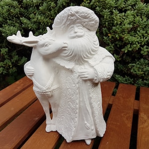 May include: White ceramic figurine of Father Christmas holding a reindeer. Father Christmas is wearing a detailed, ornate robe and a crown. The reindeer is standing on its hind legs.