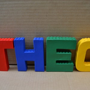 Hand painted papier mache lego letters spelling THEO in red, blue, green & yellow